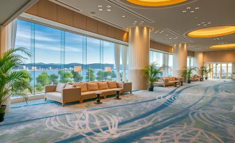 a modern lounge area with couches , chairs , and potted plants is shown with large windows overlooking the water at Hotel Ichibata