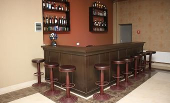 a well - stocked bar with a brown counter and red stools , surrounded by various bottles and wine glasses at Continental Hotel