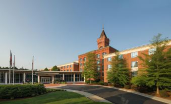 a large brick building with a clock tower , surrounded by trees and grass , under a clear blue sky at Wellsworth Hotel