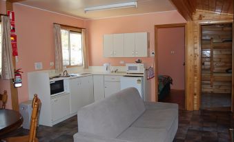a small kitchen with white cabinets , a dining table , and a couch in the living room at Gumleaves Bush Holidays
