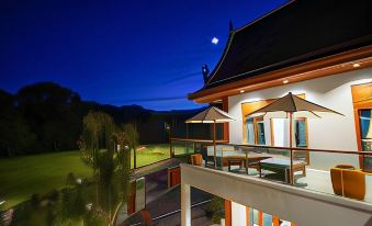 a building with a balcony and outdoor furniture is lit up at night , with a full moon in the sky at Mae Rim Grace