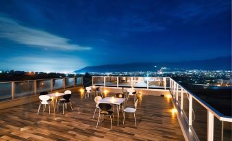 a rooftop dining area with wooden floors , white tables and chairs , and a view of the city at night at Fuefukigawa Onsen Zabou