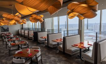 a modern restaurant with large windows , wooden tables and chairs , and orange pendant lights hanging from the ceiling at DoubleTree by Hilton Cedar Rapids Convention Complex