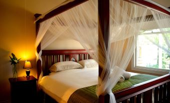 a large bed with a wooden frame and white netting is in a room with a lamp at Little River Bed and Breakfast