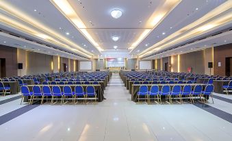 a large conference room with rows of blue chairs and tables , white walls , and a ceiling at Hotel Horison Grand Serpong