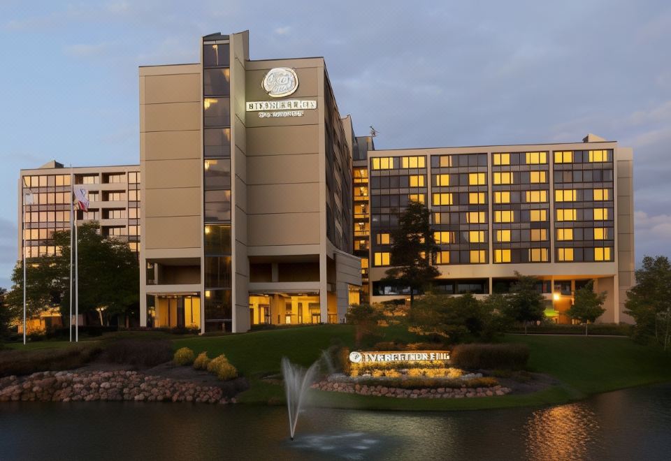 a large hotel building surrounded by trees and a lake , with a fountain in front of it at DoubleTree by Hilton Chicago - Oak Brook