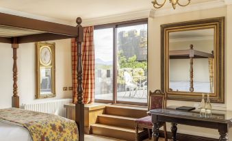 a cozy bedroom with a large window , wooden floor , and floral bedspread , featuring a desk , chair , and fireplace at Abbeyglen Castle Hotel