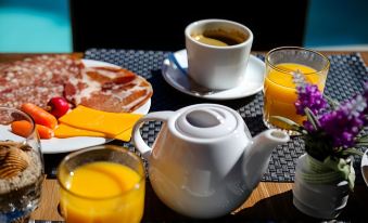a dining table with a cup of coffee , a plate of bacon , and a plate of orange juice at Hotel Restaurant de la Mer
