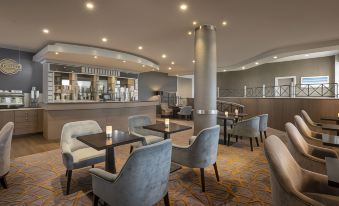 a modern , well - lit hotel lobby with comfortable seating areas and a bar area , including two chairs and a coffee table at Maldron Hotel Belfast International Airport
