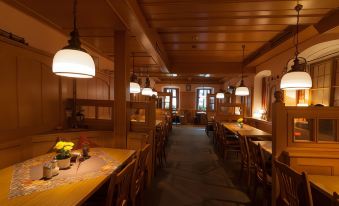 a dimly lit restaurant with wooden tables and chairs , hanging lights , and a window at the end at Akzent Hotel Schranne