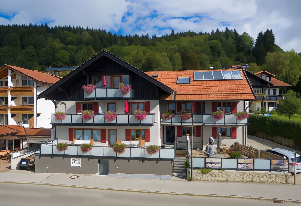a two - story building with red roofs and balconies , surrounded by greenery and situated on a street at Hotel Haus am See