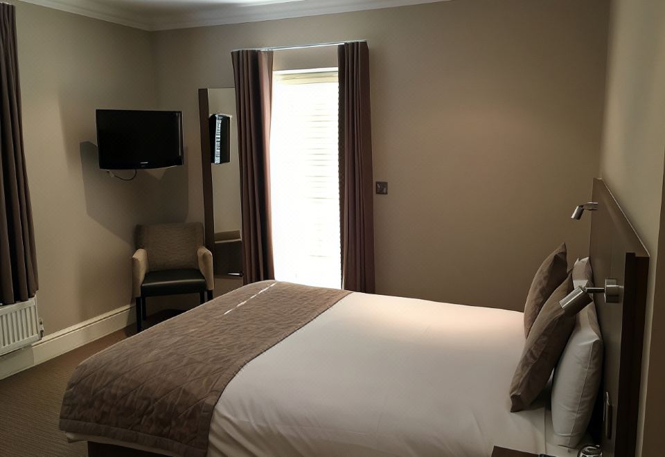 a well - lit hotel room with a comfortable bed , a tv , and a desk , all decorated in neutral colors at The Buxted Inn