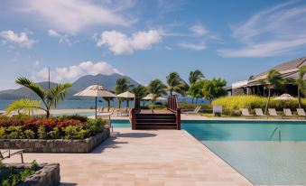 a resort with a large pool surrounded by lounge chairs and umbrellas , as well as a mountain in the background at Park Hyatt St Kitts Christophe Harbour