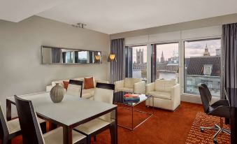 a spacious living room with a couch , chairs , and dining table is shown with large windows at Park Plaza Westminster Bridge London