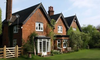 a large red brick house with black roof and chimney , surrounded by lush greenery and a green lawn at Church Farm Accomodation