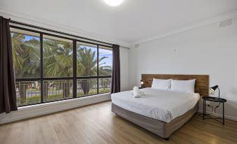 a modern bedroom with large windows , wooden flooring , and a white bed , offering a view of palm trees outside at Econo Lodge Lilydale