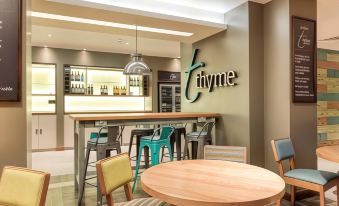 "a modern bar area with a wooden bar , stools , and a large green sign that reads "" thyme ""." at Premier Inn Penzance