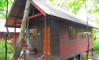 a small wooden cabin with a red door and windows , situated in a wooded area at Borneo Natural Sukau Bilit Resort