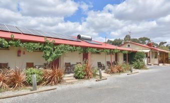 a building with a red roof and green plants is surrounded by bushes and trees at Inglewood Motel and Caravan Park Victoria