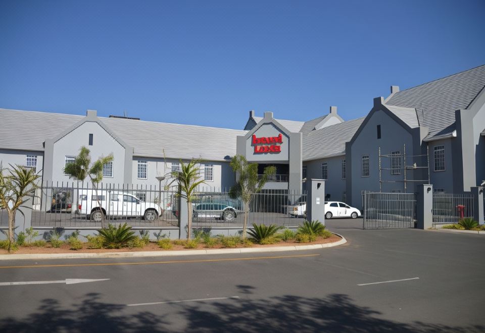 "a modern hotel building with a red sign that says "" the landmark "" and surrounded by parked cars and palm trees" at Indaba Lodge Gaborone