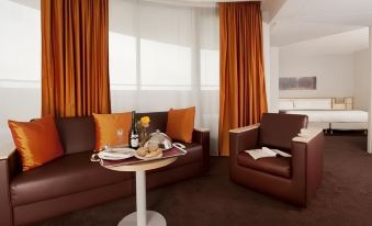 a living room with a brown couch , a chair , and a coffee table in front of orange curtains at Novotel Tours Centre Gare