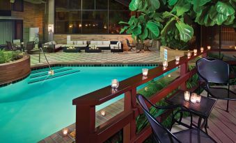 a hotel pool area with a wooden deck , potted plants , and chairs , as well as several lit candles placed around the pool at DoubleTree by Hilton Hotel Murfreesboro