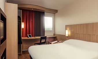 a hotel room with a large bed , a desk , a chair , and a window with red curtains at Ibis Epinay Sur Seine - Gennevilliers