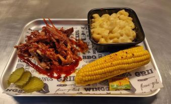 a dining table with a plate of food , including meat , corn on the cob , and macaroni at Coach House Hotel