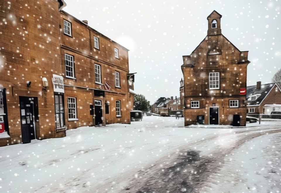 a snowy street with two buildings , one on the left and one on the right , surrounded by snow at The White Hart Hotel