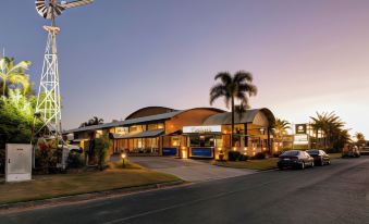 a large building with a curved roof and palm trees in front of it , set against a sunset at Windmill Motel and Events Centre