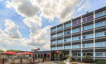 a modern building with multiple floors , surrounded by a parking lot and a clear blue sky at Ibis Lyon Villefranche Sur Saone