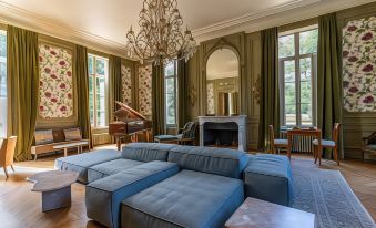 a large , elegant living room with a blue couch , multiple chairs , and a piano in the center at Les Sources de Cheverny