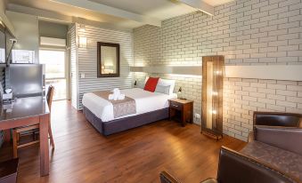 a large bed with a white headboard and footboard is in the center of a room with wooden floors and brick walls at Morwell Motel