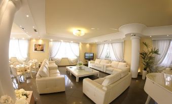 a spacious living room with white leather couches and chairs , a television , and a dining table at Hotel Luxor