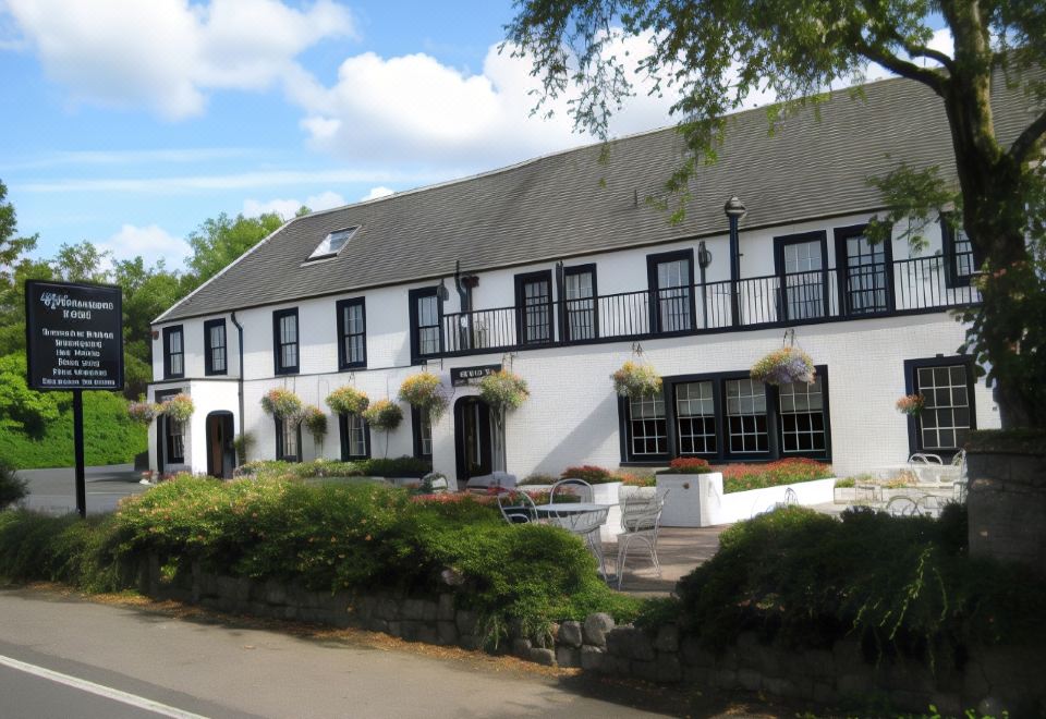 a white building with black trim and windows , surrounded by trees and flowers , under a blue sky at Uplawmoor