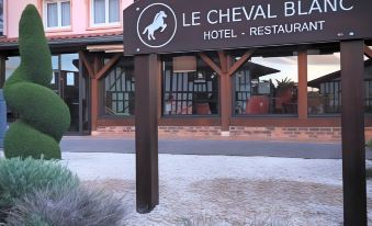 a sign for the le cheval blanc hotel and restaurant in front of a pink building , with the name displayed on it at Le Cheval Blanc - Lac du der - Logis Hotel