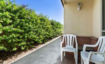 a balcony with two white chairs and a small table , surrounded by greenery and a blue sky at Emerald Explorers Inn