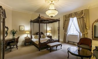 a spacious bedroom with a four - poster bed in the center , surrounded by various pieces of furniture and decorations at Doxford Hall Hotel and Spa