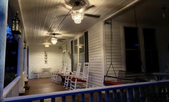 a porch with white wooden walls , blue railing , and multiple white chairs hanging from the ceiling at Whole Hearts Bed and Breakfast