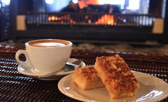 a white plate with two pieces of cake and a cup of coffee on a dining table near a fireplace at The Park Hotel Ruapehu