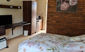 a hotel room with a large bed , a bathroom , and a kitchen area , decorated with flowers and a clock at Toora Lodge Motel