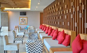 a modern lounge area with wooden paneling , red pillows on the back of chairs , and a couch with zigzag patterned cushions at FamVida Hotel Lubuklinggau Powered by Archipelago