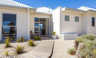 a modern , white house with a wooden deck and potted plants on either side of the entrance at Saltwater - Absolute Oceanfront, Hot Tubs, Sauna, Fire Pits