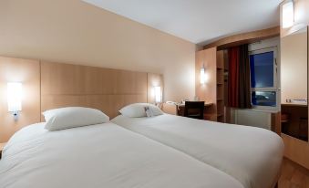 a hotel room with two beds , one on the left side of the room and the other on the right side at Ibis Clermont-Ferrand Sud Carrefour Herbet