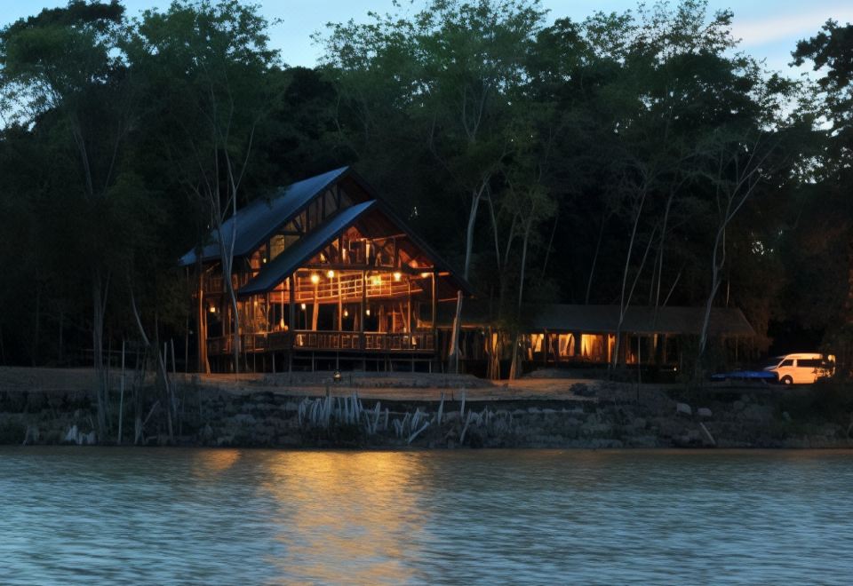 a wooden building is situated on the shore of a lake at night , illuminated by lights at Borneo Natural Sukau Bilit Resort