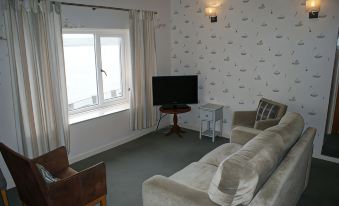 a cozy living room with a beige couch , a wooden coffee table , and a television mounted on the wall at Ferry House Inn