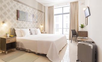 a large bed with white linens is in a room with a window and a suitcase at Alexandra Hotel
