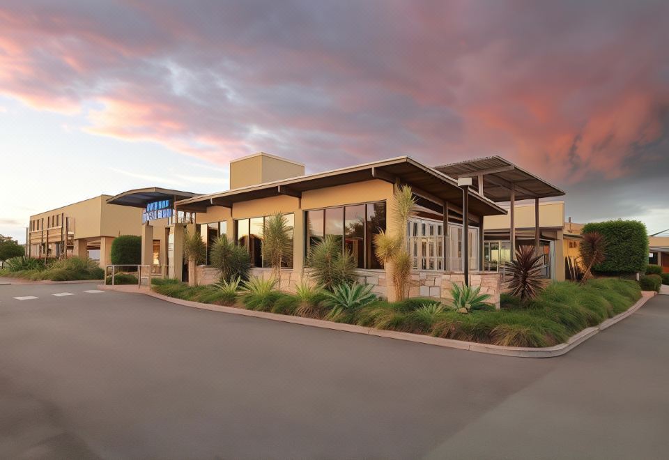 a modern building with a glass facade , surrounded by lush greenery and a sunset sky at Everton Park Hotel