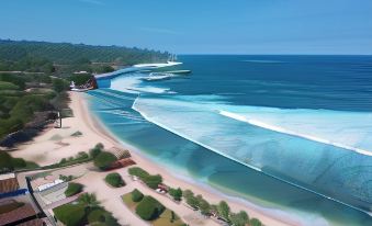 a panoramic view of a tropical beach with white waves and clear blue water , surrounded by lush greenery at The Royal Joglo