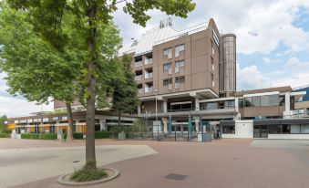 a modern building with multiple floors and balconies , situated next to a tree - lined path in an urban setting at Leonardo Hotel Lelystad City Center